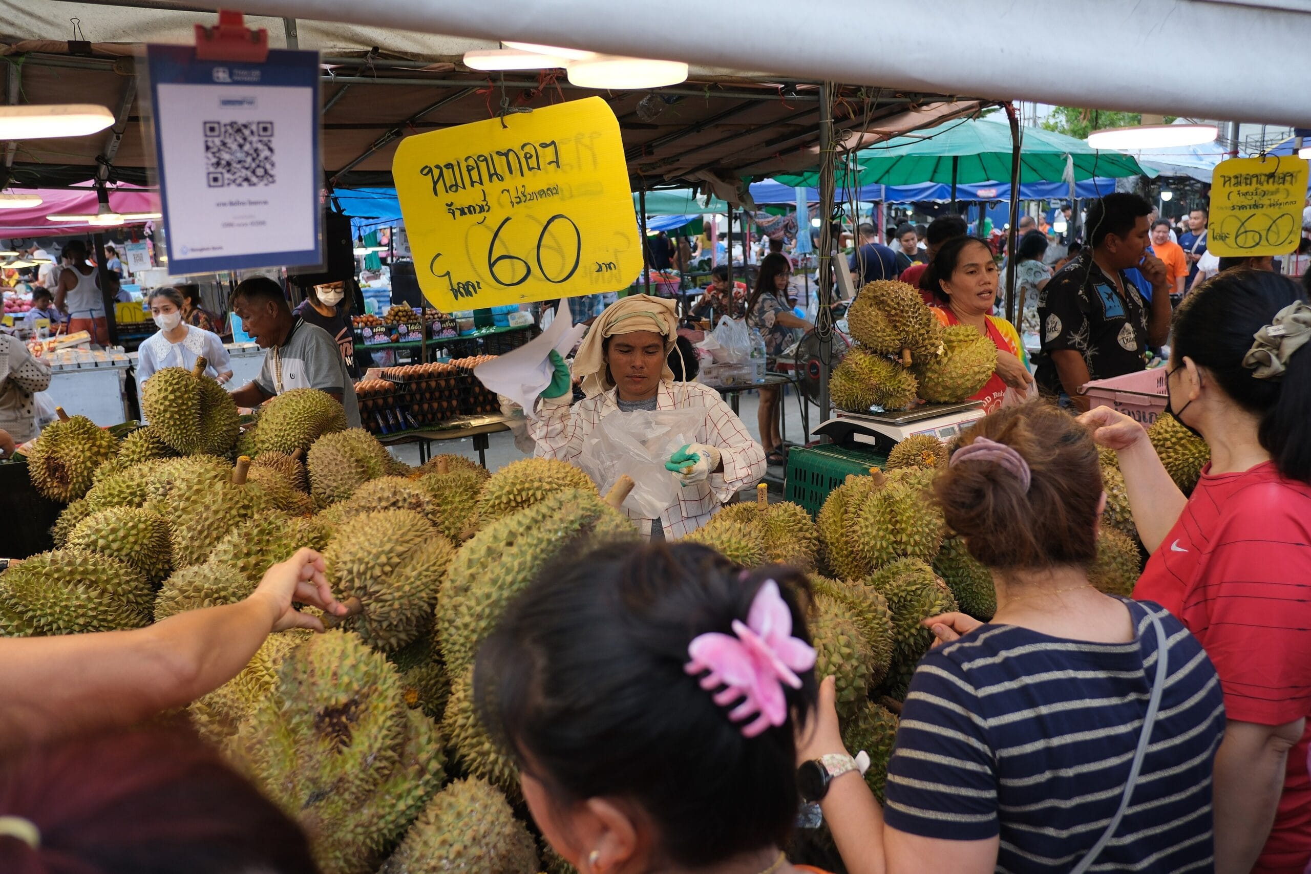 A Thai market stall piled with durian at 60 baht as shoppers inspect the fruit