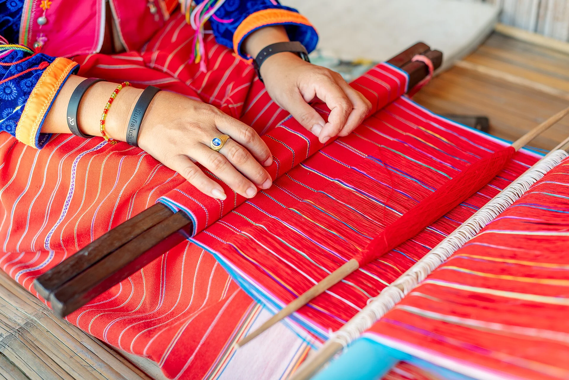 A Karen woman weaving bright red textile on a traditional loom in northern Thailand