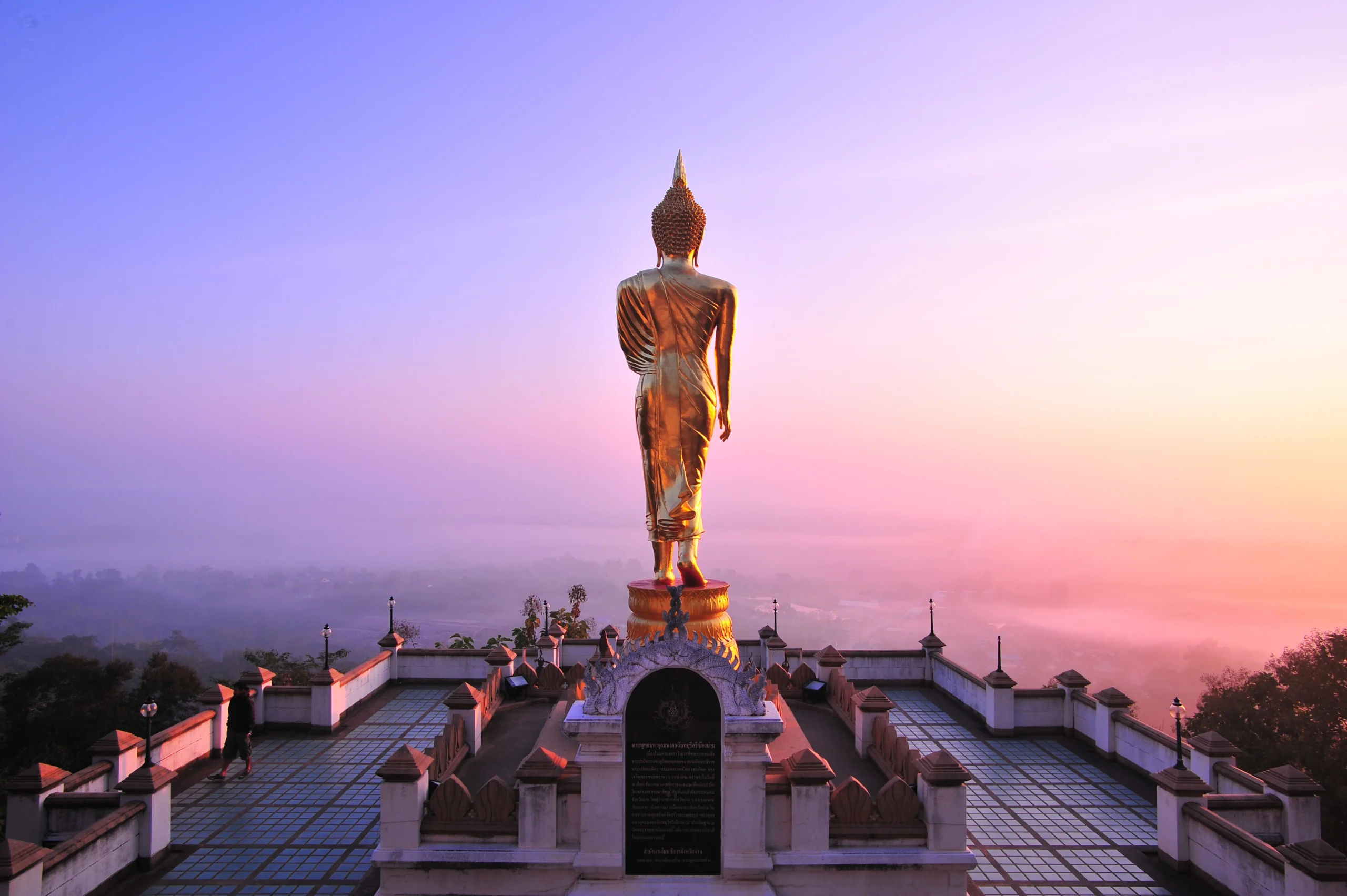 Golden standing Buddha at Wat Phra That Khao Noi overlooking Nan town at sunset