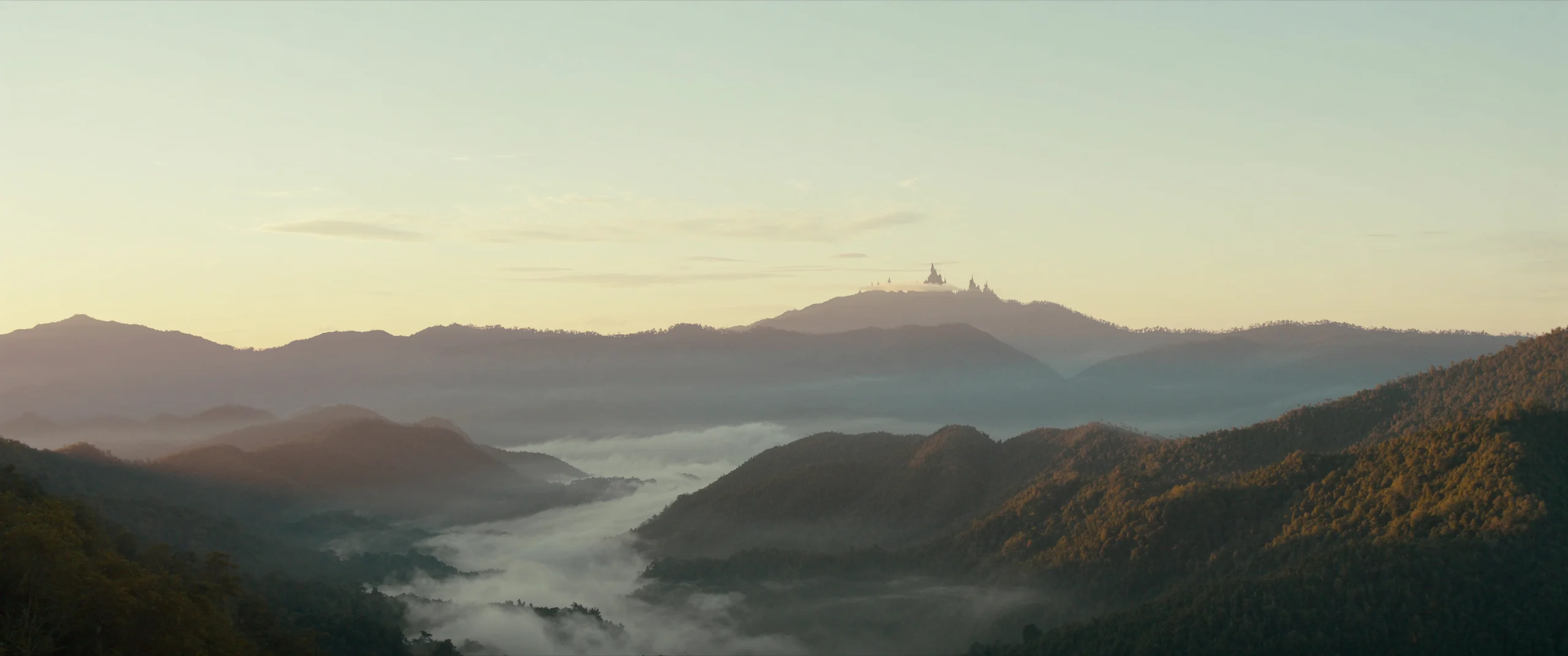 Misty forested valleys at dawn with a golden hilltop temple, northern Thailand