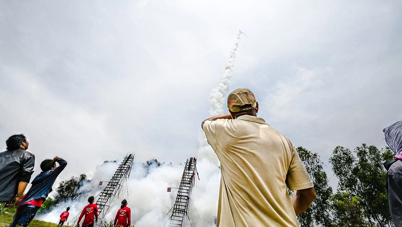 Crowd watching a home-made rocket launch with a smoke trail during Bun Bang Fai in Yasothon