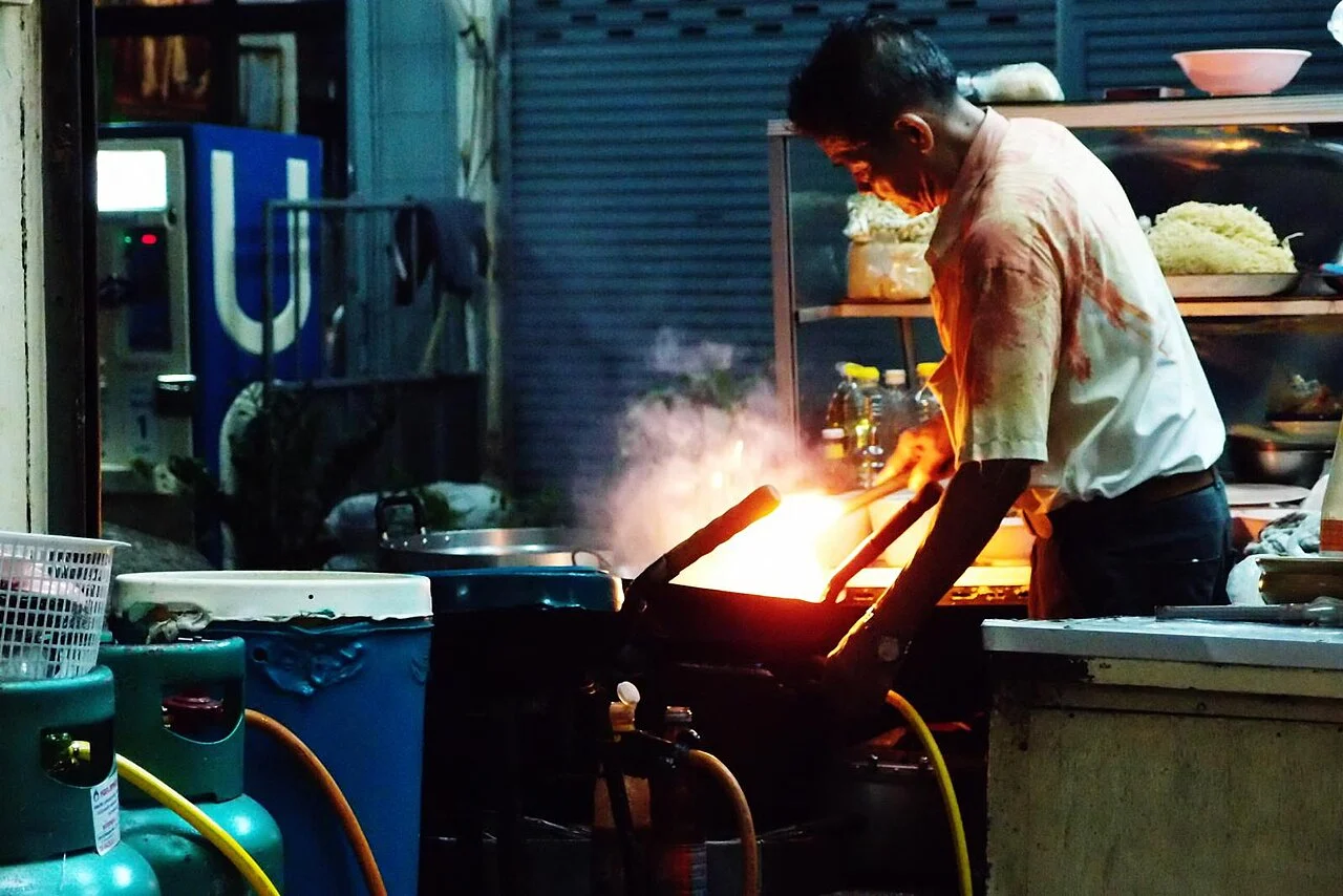 Street food cook working a flaming wok at a Bangkok night stall