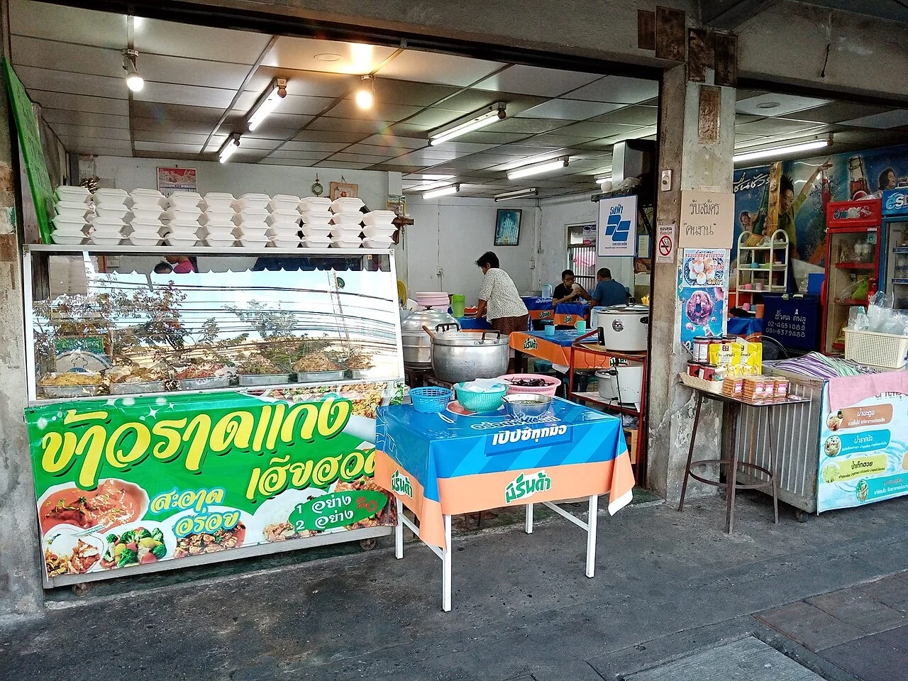 Khao gaeng shopfront in Bangkok with curry trays behind glass and a sign listing one- and two-topping prices