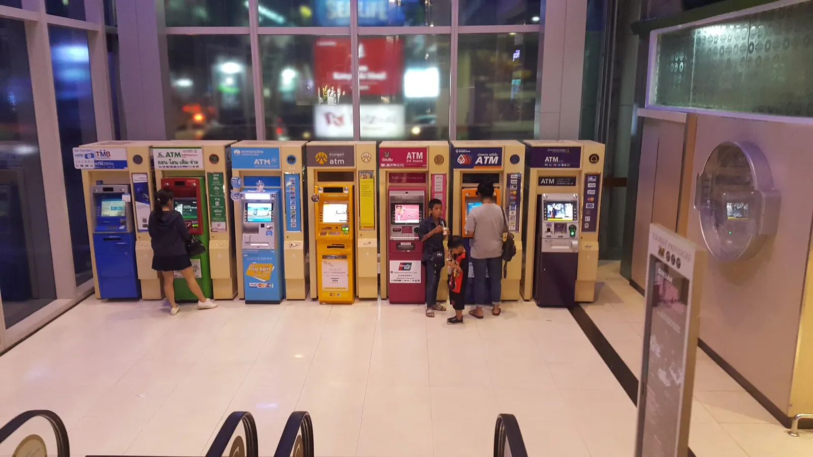 A row of brightly coloured ATMs from different Thai banks lined up inside a Bangkok shopping mall