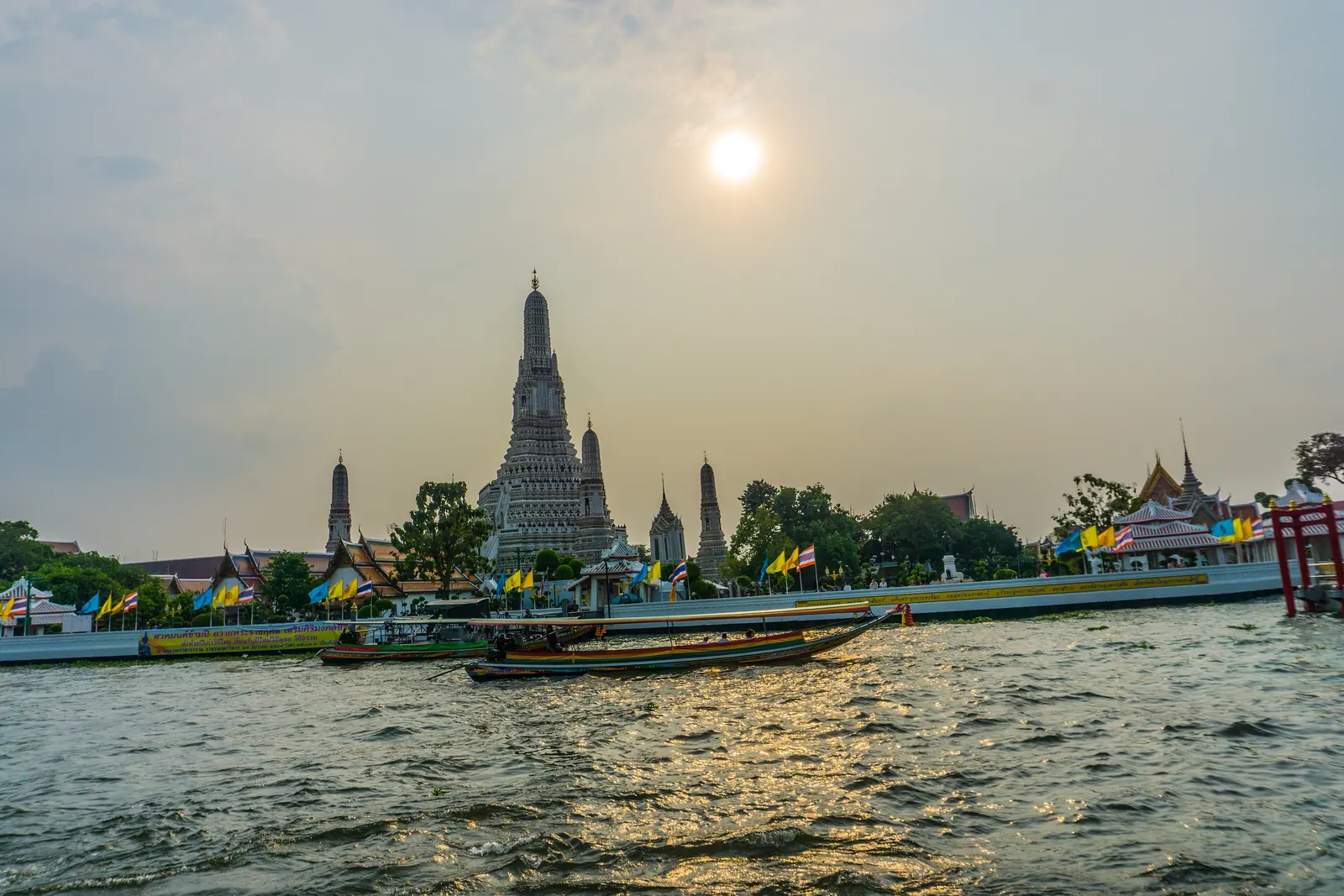 Wat Arun at sunset seen from the Chao Phraya River, a longtail boat passing in front