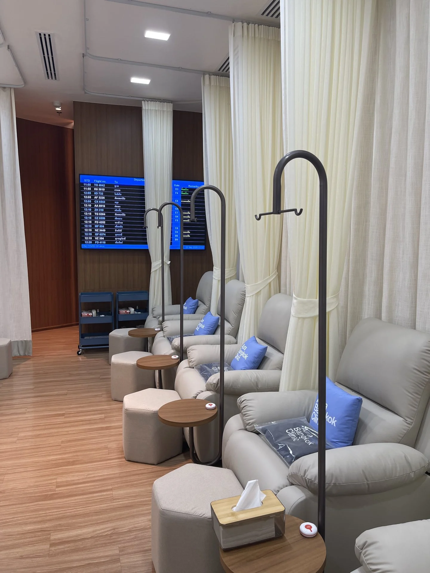 IV drip lounge with curtained recliners and a departures board at Aura Bangkok Clinic Suvarnabhumi Airport