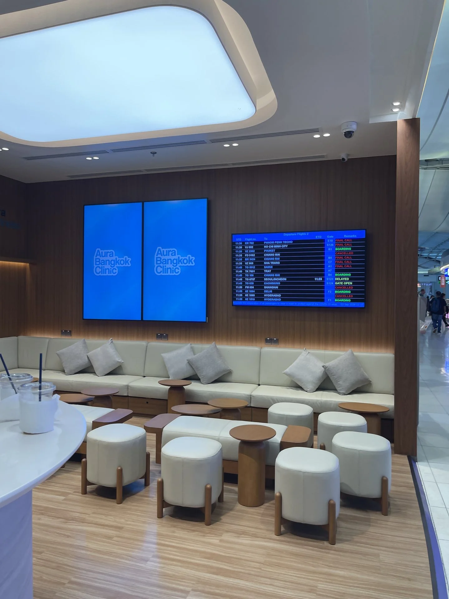 Waiting lounge with sofas and a live flight information display at Aura Bangkok Clinic Suvarnabhumi Airport