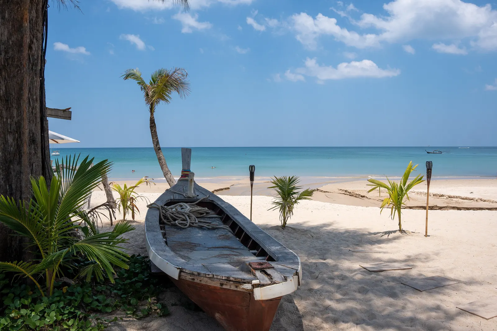 A beached wooden boat and palms on Bang Tao Beach, Phuket, a long flat stretch of sand