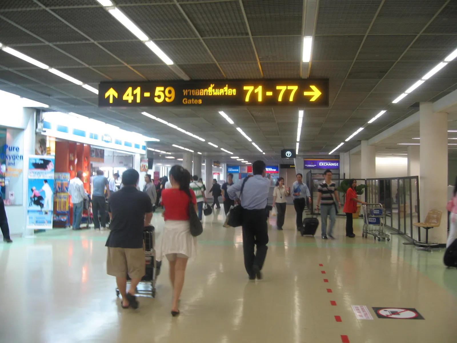 A long low corridor inside Terminal 2 at Don Mueang Airport, Bangkok, with gate signs overhead