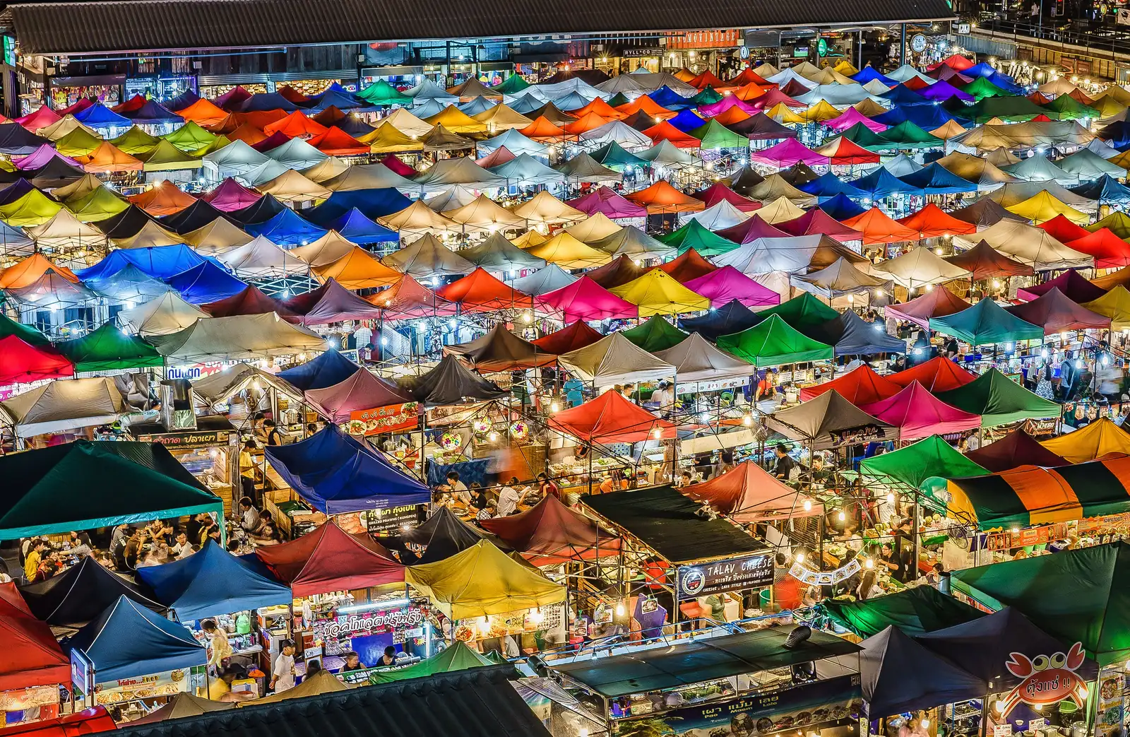 Bangkok night market from above: rows of lit stall roofs and crowds after dark