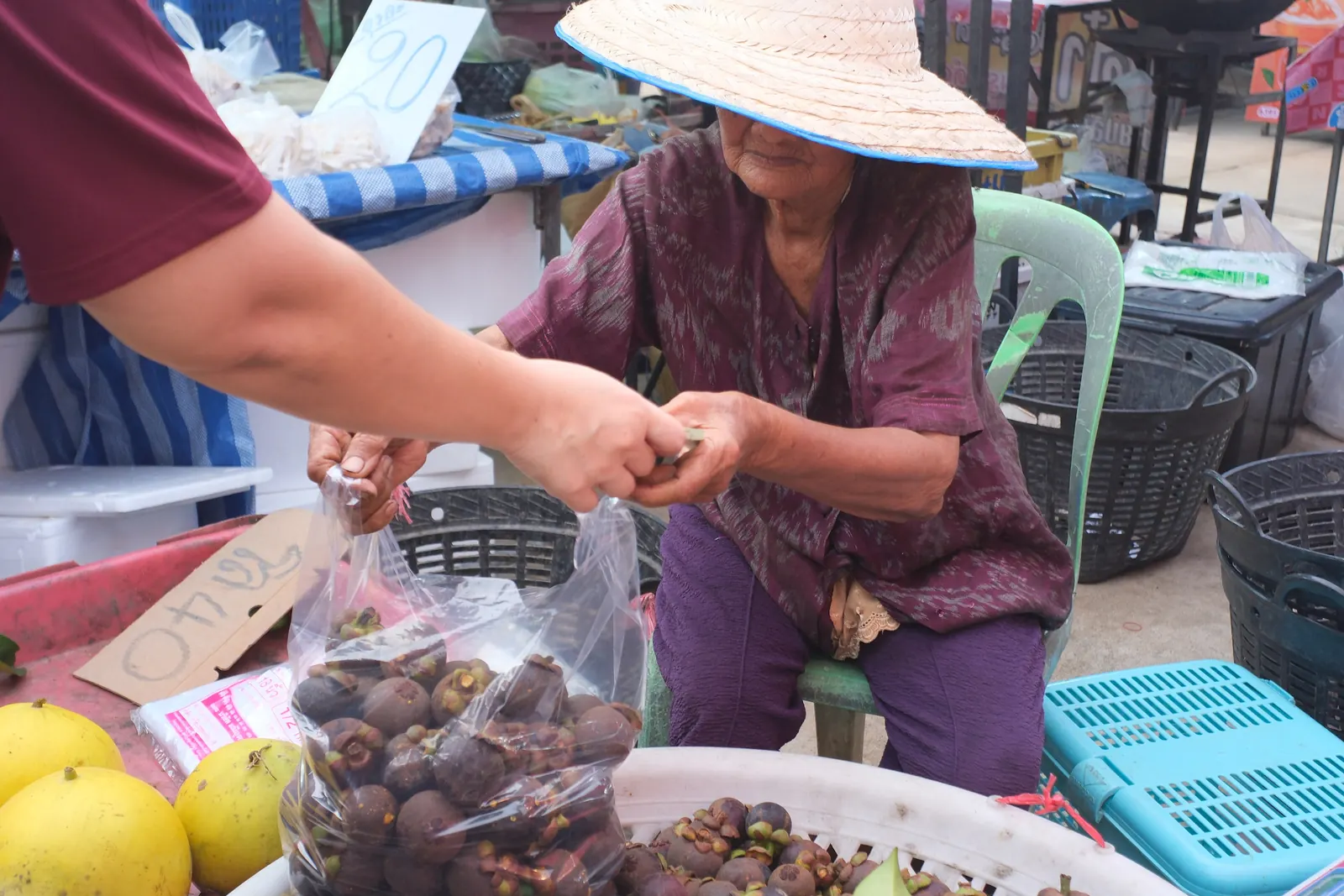 A market vendor in a straw hat selling mangosteens by the bag in Thailand