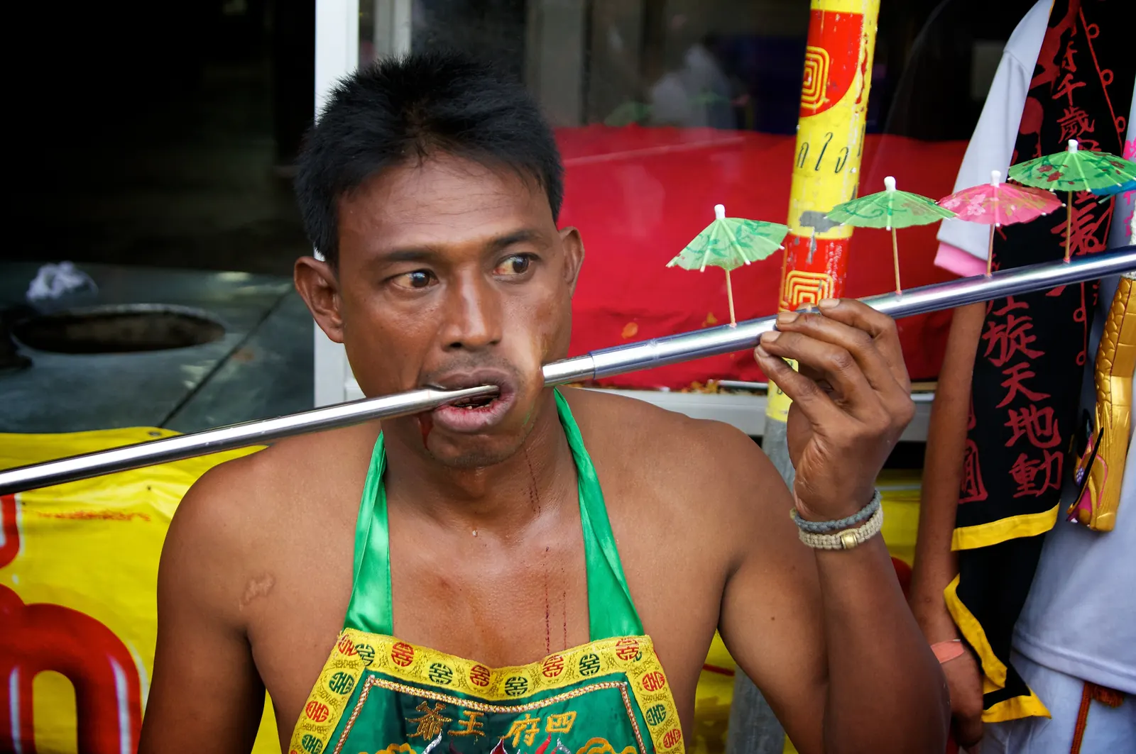 Ma song with a skewer through his cheek walking under umbrellas in a Jui Tui shrine procession, Phuket