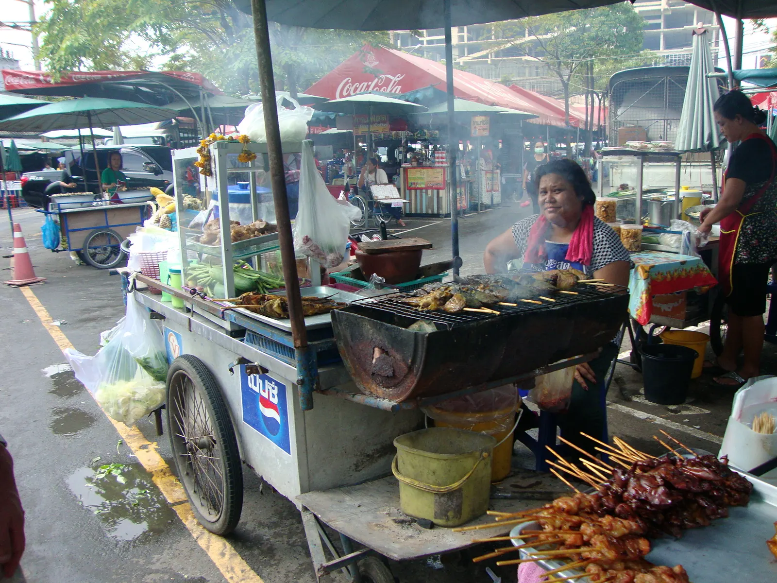 Bangkok street food cart grilling skewers on the pavement