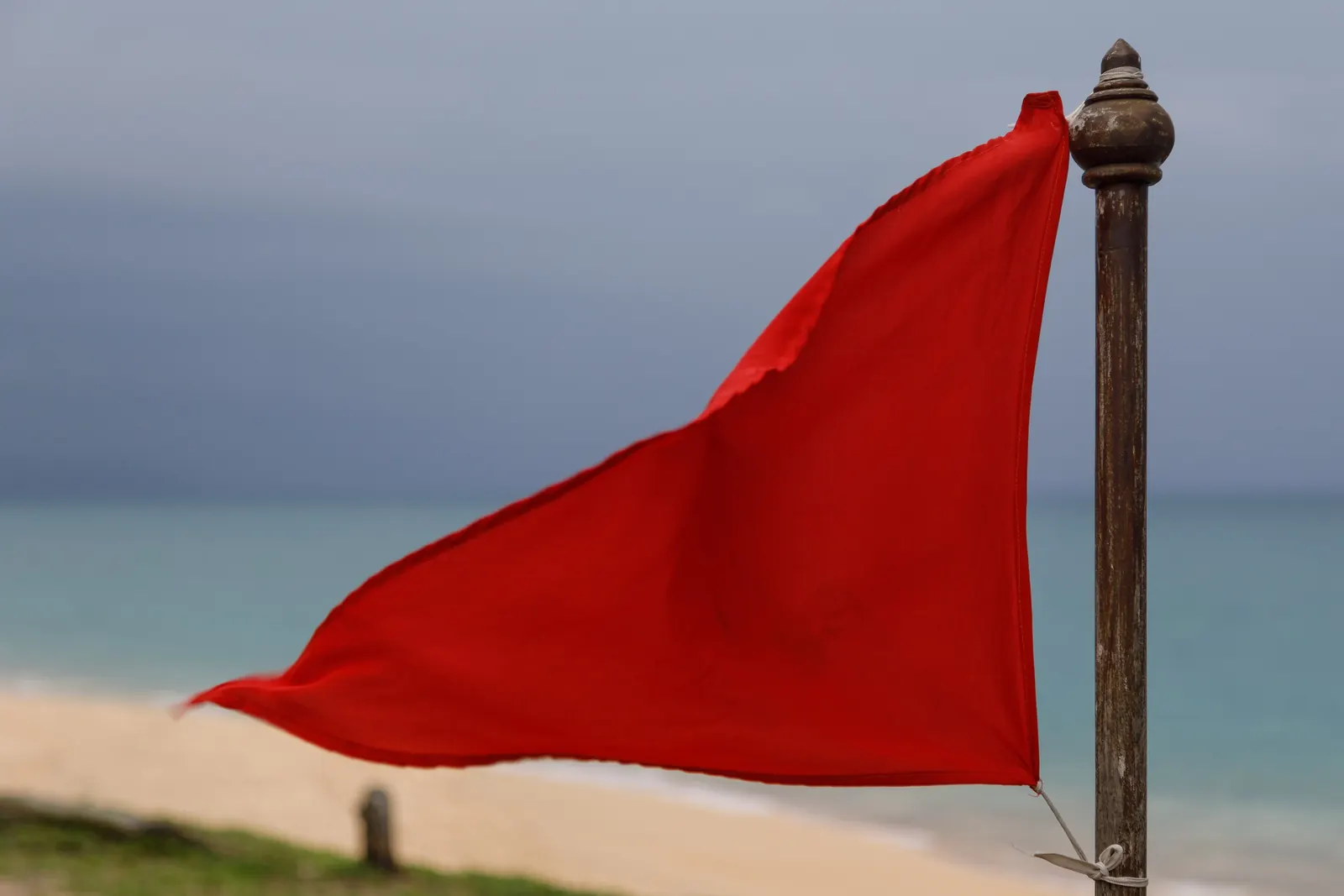 A red warning flag on Mai Khao Beach, Phuket, with the Andaman surf behind it