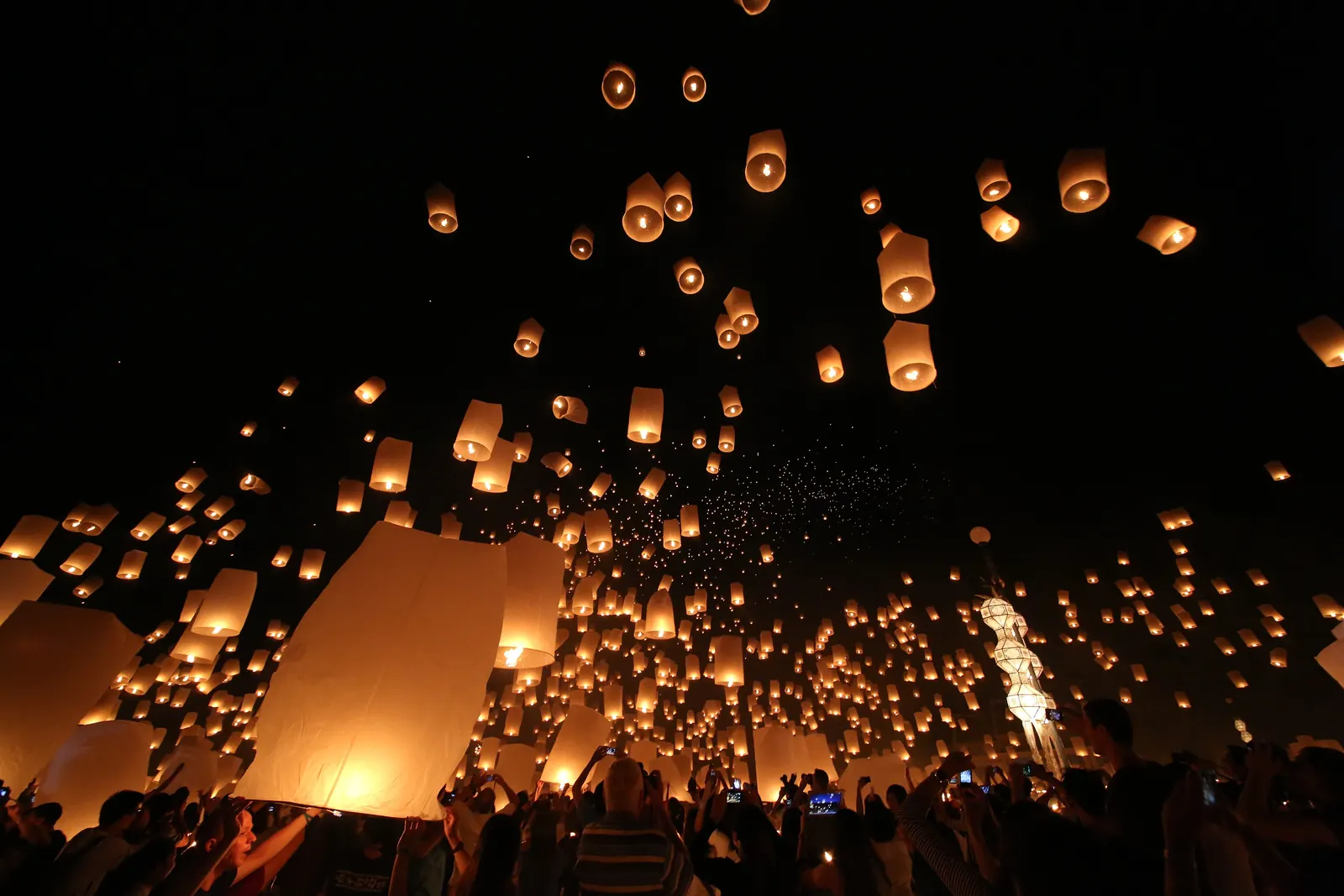 Thousands of sky lanterns rising over a crowd near Chiang Mai during Yi Peng