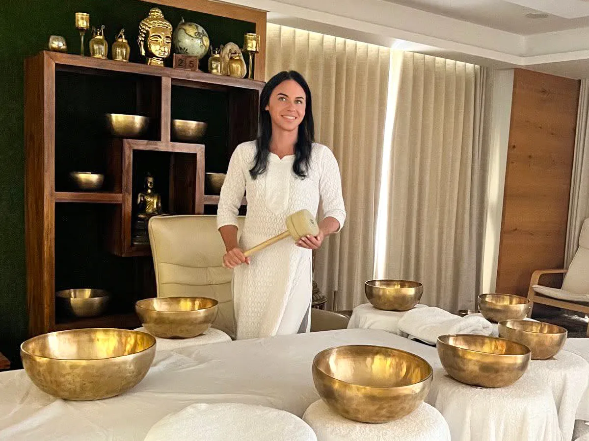 Sound therapist Svetlana Kaivalya standing behind a table of Tibetan singing bowls holding a mallet